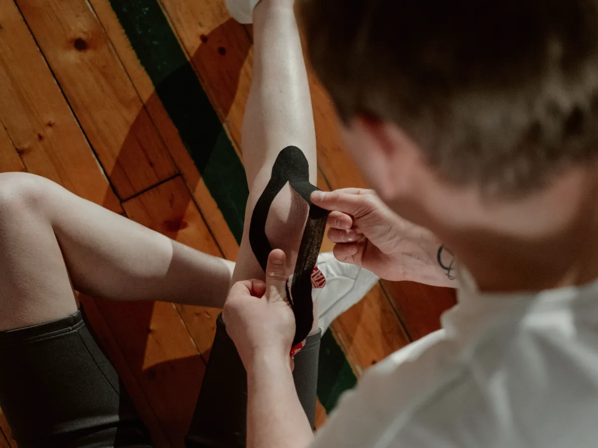 A physiotherapist applying kinesiology tape to an athlete's leg.